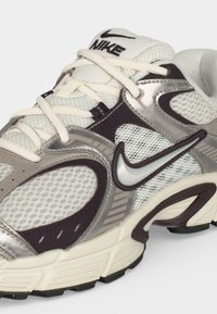 Λευκό και γκρι sneaker Nike με πλέγμα, κρέμ κορδόνια και σκουρόχρωμες λεπτομέρειες, με εμφανές ασημί λογότυπο Nike swoosh.