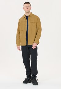 Langarm, knoopsluiting overhemd in mosterdgeel, met twee borstzakken, gecombineerd met zwarte broek en zwarte laarzen. Glad textuur.
