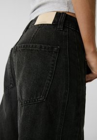 Czarne dżinsy z wysokim stanem, z dwiema tylkimi kieszeniami, skórzaną łatą na pasku i lekko teksturowanym wykończeniem.