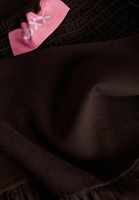 Μαύρο ύφασμα με πιεσμένες ραφές κοντά σε ροζ ετικέτα ρούχου με λευκό μερικώς ορατό κείμενο.