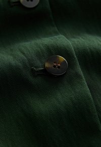 Mørkegrønt stof med en tekstureret overflade, der har en rund, mørk knap med fire huller fastgjort, som fremhæver fine syninger.