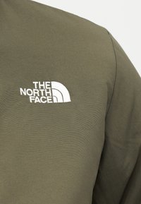 Olivenasto zelena tkanina z belo vezenim napisom "THE NORTH FACE" in polkrožnim motivom na zgornji levi strani.