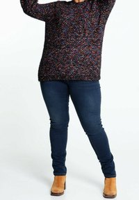 Svart texturerad tröja med flerfärgade prickar, ihopparad med mörkblå skinny jeans och bruna ankelstövlar. Tröjan har lång ärm.