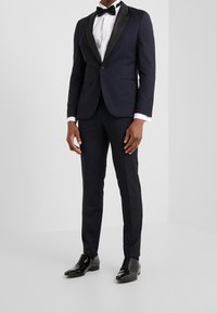 Tuxedo a fantasia navale con rever a punta in satin nero, camicia bianca e papillon nero, completato da scarpe in pelle nera lucida.
