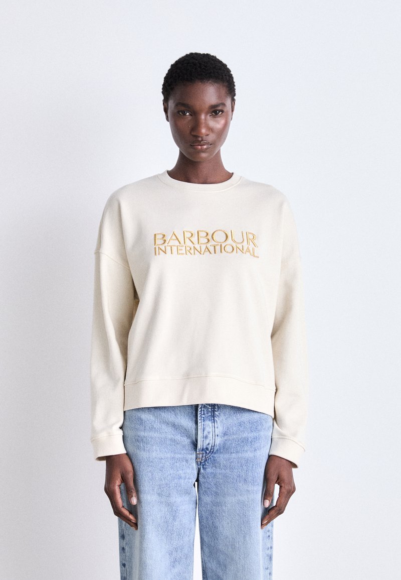 Krém színű pulóver, lekerekített nyakkal és ejtett vállakkal, sárga hímzett "BARBOUR INTERNATIONAL" felirattal az elején.