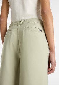 Pantaloni a gamba larga verde chiaro con una texture liscia, dotati di tasche posteriori e di un piccolo etichetta con logo vicino alla vita.