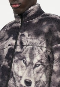Φλις μπουφάν με γραφική εκτύπωση λύκου σε γκρί αποχρώσεις, ψηλό γιακά και πλήρη φερμουάρ με μαύρη περιτονία. Μαλακή υφή και χαλαρή εφαρμογή.