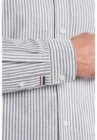 Szara i biała koszula w paski, z mankietem na guziki z małym czerwonym i granatowym paskiem, wykonana z tkaniny tkanej.