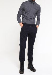 Dunkelgrauer Rollkragenpullover, figurbetont, kombiniert mit navyblauen Hosen. Schwarze Schnürstiefel mit strukturierten Sohlen. Lässiges Outfit geeignet für kühleres Wetter.