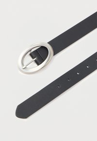 Svart lærbelte med oval, blank sølvspenne liggende flatt med synlige hull på hvit bakgrunn.