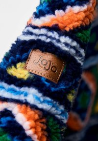 Tessuto colorato e tattile con fibre simili alla lana in blu, arancione, verde e giallo; etichetta in pelle marrone con "JoJo" impresso.