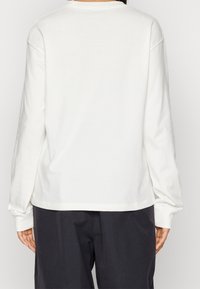 Langärmliges, Rundhals-T-Shirt aus off-white Baumwolle mit lockerer Passform, gerippten Bündchen und glatter Textur. Schlichte Rückseite, ohne Muster oder Akzente.