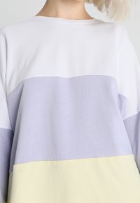 Wygodna bluzka z długim rękawem w kolorze białym, lawendowym i jasnym żółtym w wzór color-block; miękki materiał; dekolt w łódkę bez widocznych zapięć.
