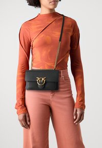 Black leather crossbody bag with a gold-toned hardware accent, featuring a flap closure and chain shoulder strap. Textured surface adds detail.
