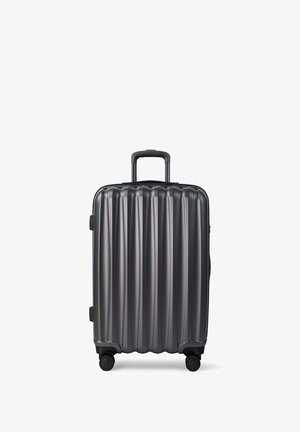 Czarna, twarda walizka z pionowymi żłobieniami, z teleskopowym uchwytem i czterema obrotowymi kółkami, stojąca w pionie na białym tle.