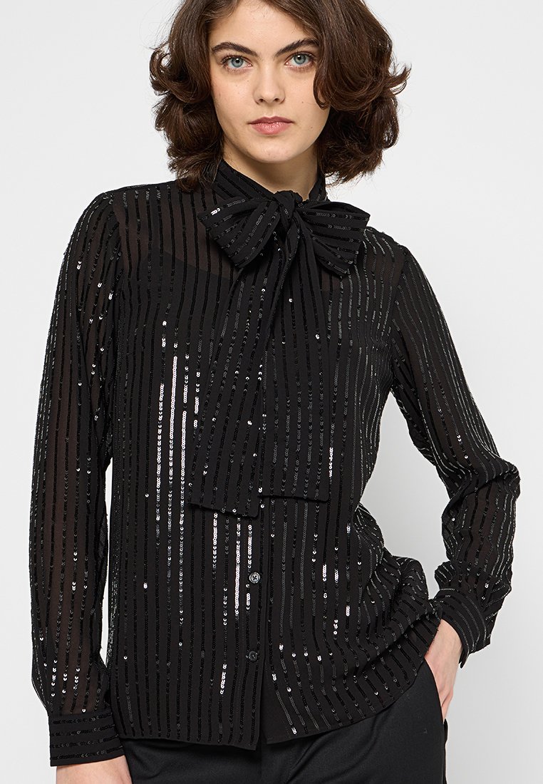 Zwarte doorschijnende blouse met verticale strepen van pailletten, strikdetail bij de kraag, lange mouwen en knopen aan de voorkant. Textuur en lichtgewicht materiaal.