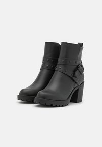 Bottines noires à talons avec une finition en cuir texturé, un épais talon haut, des sangles cloutées et un détail de boucle. Bout arrondi et semelle en caoutchouc robuste.