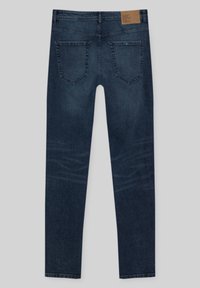 Jeans skinny de mezclilla azul oscuro con un acabado texturizado, con un parche de cuero marrón, cinco bolsillos y costuras en contraste.