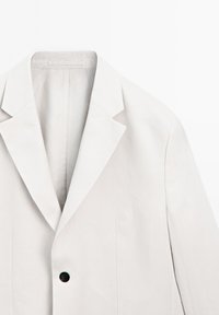 Hellgrauer Blazer aus Leinen mit Reverskragen, einem schwarzen Knopf und vertikalen Nahtdetails, mit einer glatten Textur.