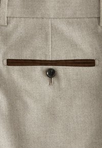 Stof de herringbone bejuc, cu o textură netedă, având o margine din catifea maro închis și un detaliu cu un buton rotund negru pe buzunarul din spate.