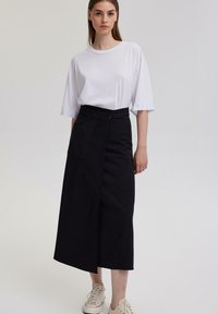 Černá midi sukně s překládaným designem a boční kapsou, spárovaná s volným bílým tričkem. Pohodlné tenisky dokončují outfit.