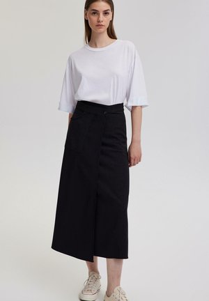 Černá midi sukně s překládaným designem a boční kapsou, spárovaná s volným bílým tričkem. Pohodlné tenisky dokončují outfit.