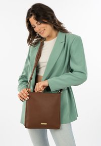 Bruine leren handtas met gestructureerde afwerking, schouderriem, gouden metalen accenten en rechthoekige vorm. Gestyled met een mintgroene blazer.