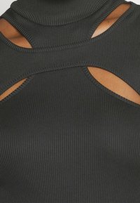 Top negro de canalé con cuello alto, que presenta detalles de cortes y una tela texturizada. El diseño resalta las líneas verticales y la exposición de la piel en los laterales.