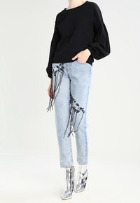 Sudadera negra de gran tamaño, jeans de mezclilla azul claro con bordado negro, y botines plateados brillantes. Ajuste holgado y detalles de tela texturizada.