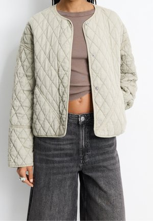 Personne portant une veste matelassée beige clair sur un haut court marron côtelé, associée à un jean large noir délavé taille haute.