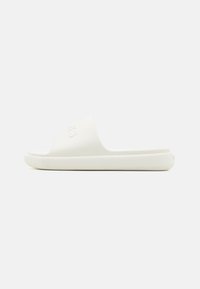 White slip-on sandal with a textured strap, flat sole, and subtle branding on the upper. Smooth finish, lightweight design.