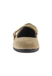 Zapato plano de ante beige con punta redondeada, tira elástica y suela de goma negra, con una pequeña hebilla decorativa en el costado.