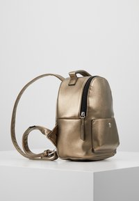 Metallischer Gold-Rucksack mit abgerundeter Form. Verfügt über eine vordere Reißverschlusstasche, verstellbare Träger und eine glatte, glänzende Textur.