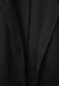 Närbild av en svart blazer med detaljerad vy av slag och krage som visar den släta tygtexturen och skräddarsydda sömmar.