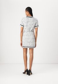 Short-sleeve dress with black and white textured check pattern, fitted waist, fringe hem, and contrasting black accents. Paired with black heels.