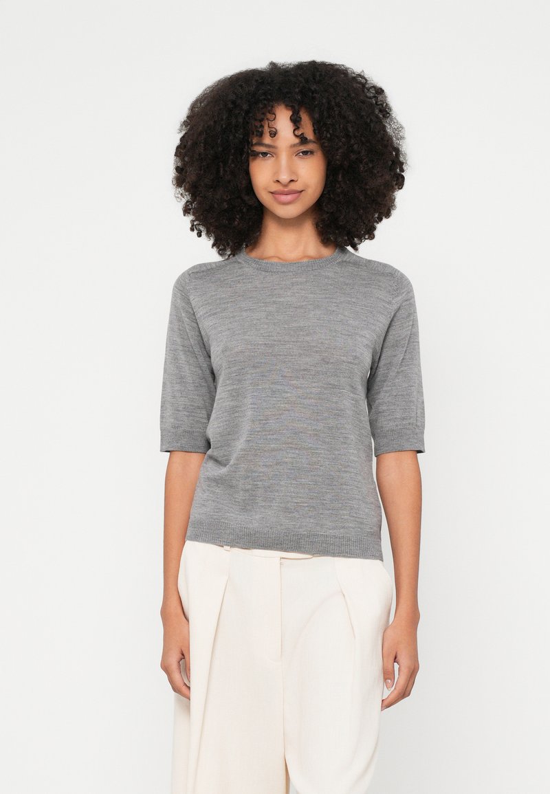 Hall triiksärk, lühikeste varrukatega, ümmarguse kaelusega, sileda tekstuuriga ja peente tooni variatsioonidega, kantud heledate õmmeldud pükstega.