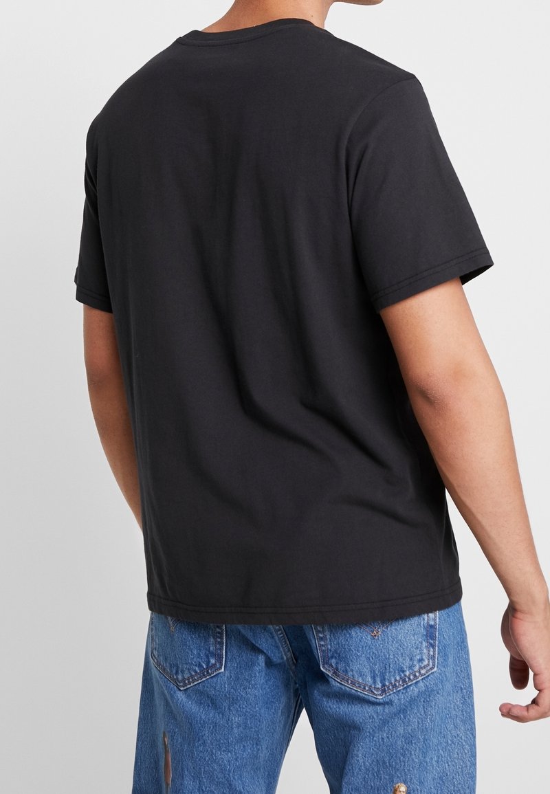 Camiseta negra de manga corta con cuello redondo, hecha de algodón. Textura suave, corte relajado y sin marcas ni adornos visibles.