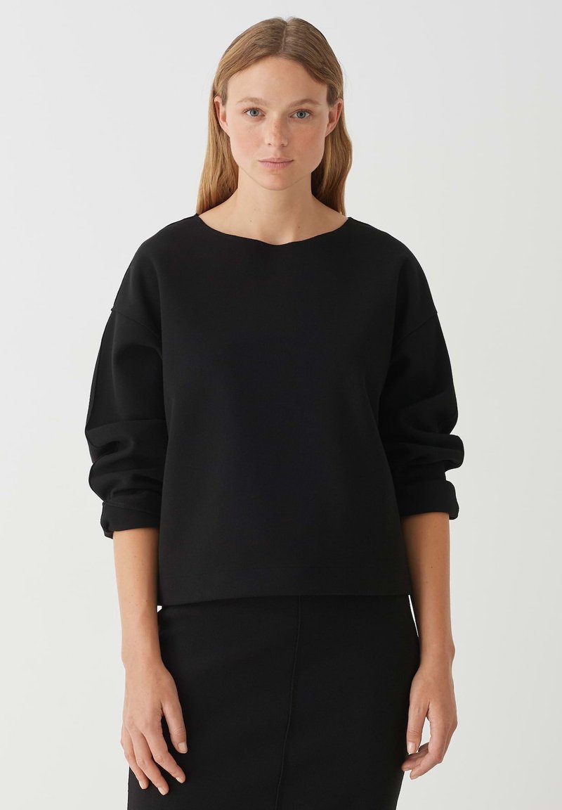 Zwarte sweatshirt met een ronde hals en oversized mouwen. Zachte textuur, relaxte pasvorm, gecombineerd met een bijpassende zwarte rok.
