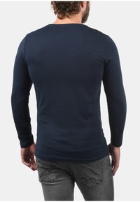 Marineblå langærmet T-shirt lavet af blødt bomuld, med en rund halsudskæring og en tætsiddende pasform. Glat tekstur og ensartet overflade uden mønstre.