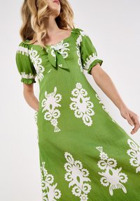 Grünes Kleid mit quadratischem Ausschnitt, gebundenem Schleifendetail, kurzen Puffärmel und einem floral-weißen Druck mit kunstvollen Mustern.