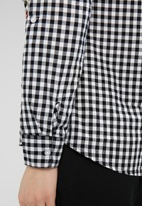 Svart och vit rutigt skjorta med långa ärmar, med knäppning vid ärmsluten och en slät tygkvalitet.