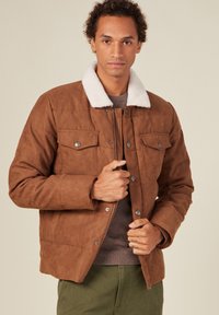 Brun mockajacka med vit fårskinnskrage, knappstängning framtill och två bröstfickor. Mjuk textur, quiltad design och varm look.