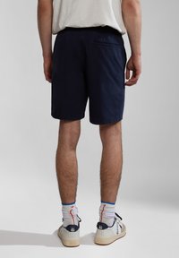 Navy blue shorts with an elastic waistband, single back pocket, and a casual fit. Paired with white sneakers and crew-length socks.