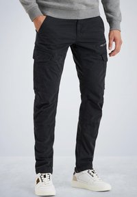 Schwarze Cargo-Hosen mit mehreren Taschen, einer lockeren Passform und einem strapazierfähigen Baumwollmix. Kombiniert mit weißen und beige Sneakers.