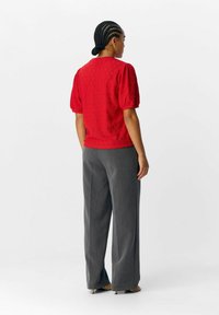 Rød tekstureret bluse med puffærmer, parret med grå brede bukser. Blusen har et blomstermønster og en rund halsudskæring.