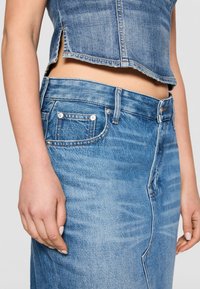 Falda de mezclilla en azul claro, con una cintura alta, bolsillos frontales y un desvanecimiento sutil. Incluye costuras visibles y un detalle de abertura lateral.