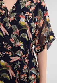 Kwiatowa sukienka rozkloszowana w granatowym kolorze z krótkimi rękawami, z misternymi wzorami ptaków i liści w odcieniach różu, zieleni i żółci. Teksturowany materiał.