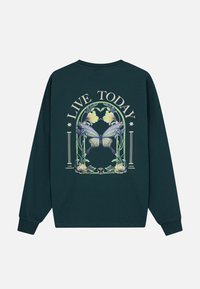 Donkergroene langemouwen t-shirt met een vlinder- en bloemenafbeelding, met de tekst "LEEF VANDAAG" in een gebogen lay-out.