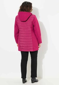 Fuchsia padded coat with a hood, featuring a textured back panel and smooth front. Worn over black pants and ankle boots.
