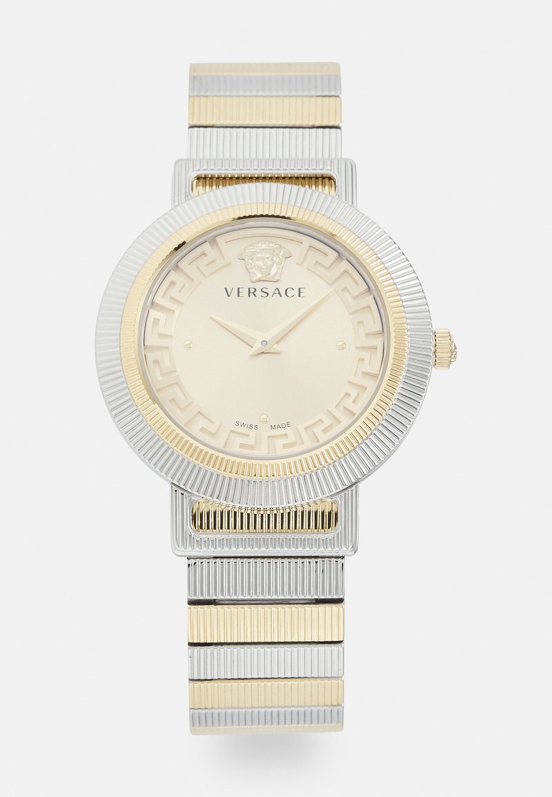 Arany és ezüst árnyalatú Versace karóra texturált kerek számlappal, Medúza logóval, görög kulcs mintával és láncból készült fém szíjjal.
